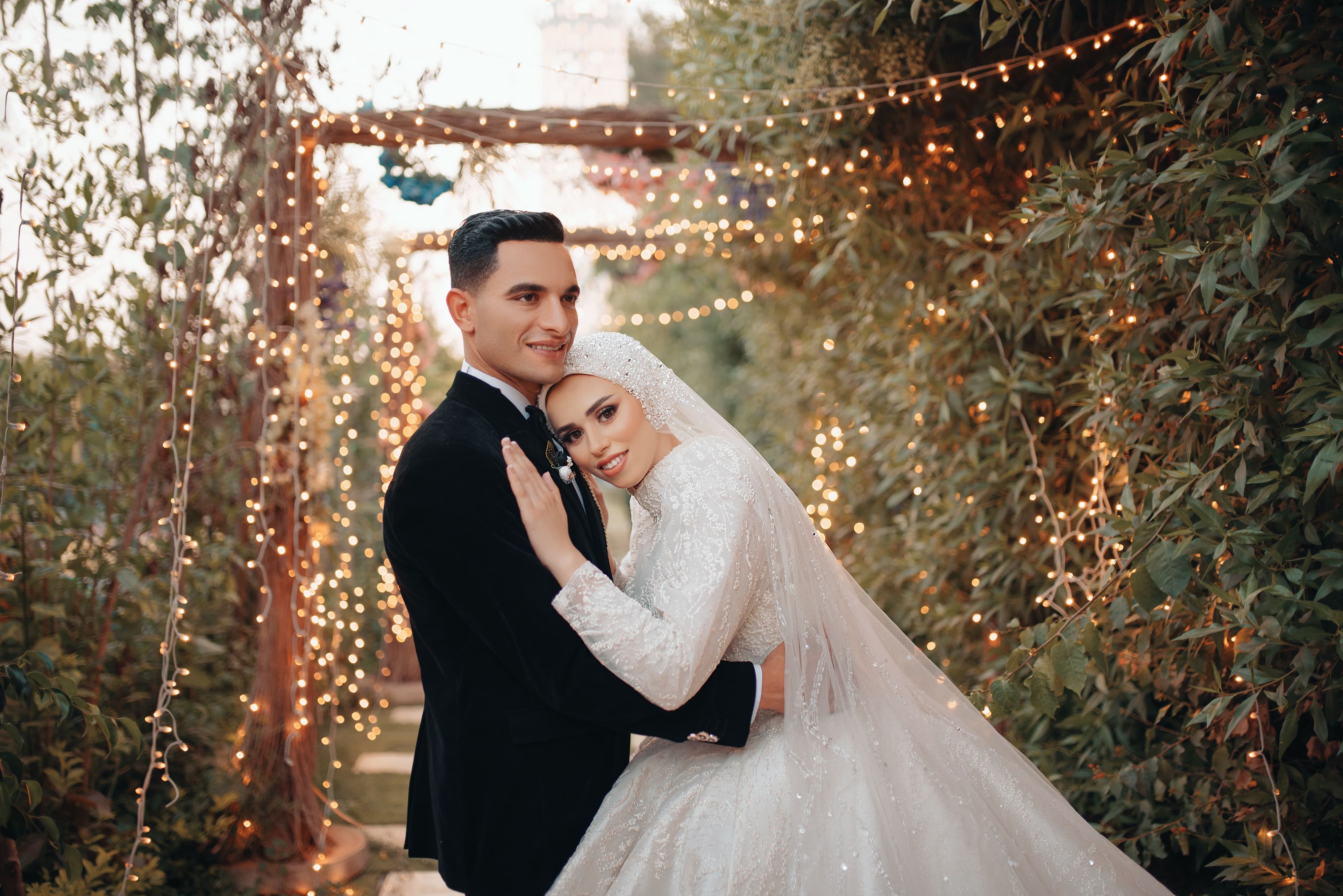 A sample photograph: a bride and groom embracing in a garden strung with lights